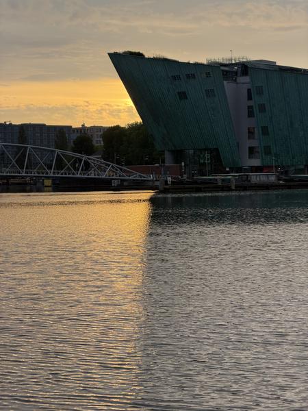 The photo captures a serene evening scene at Prins Hendrikkade, Centrum, Amsterdam, with the distinctive green-patina NEMO Science Museum prominently featured